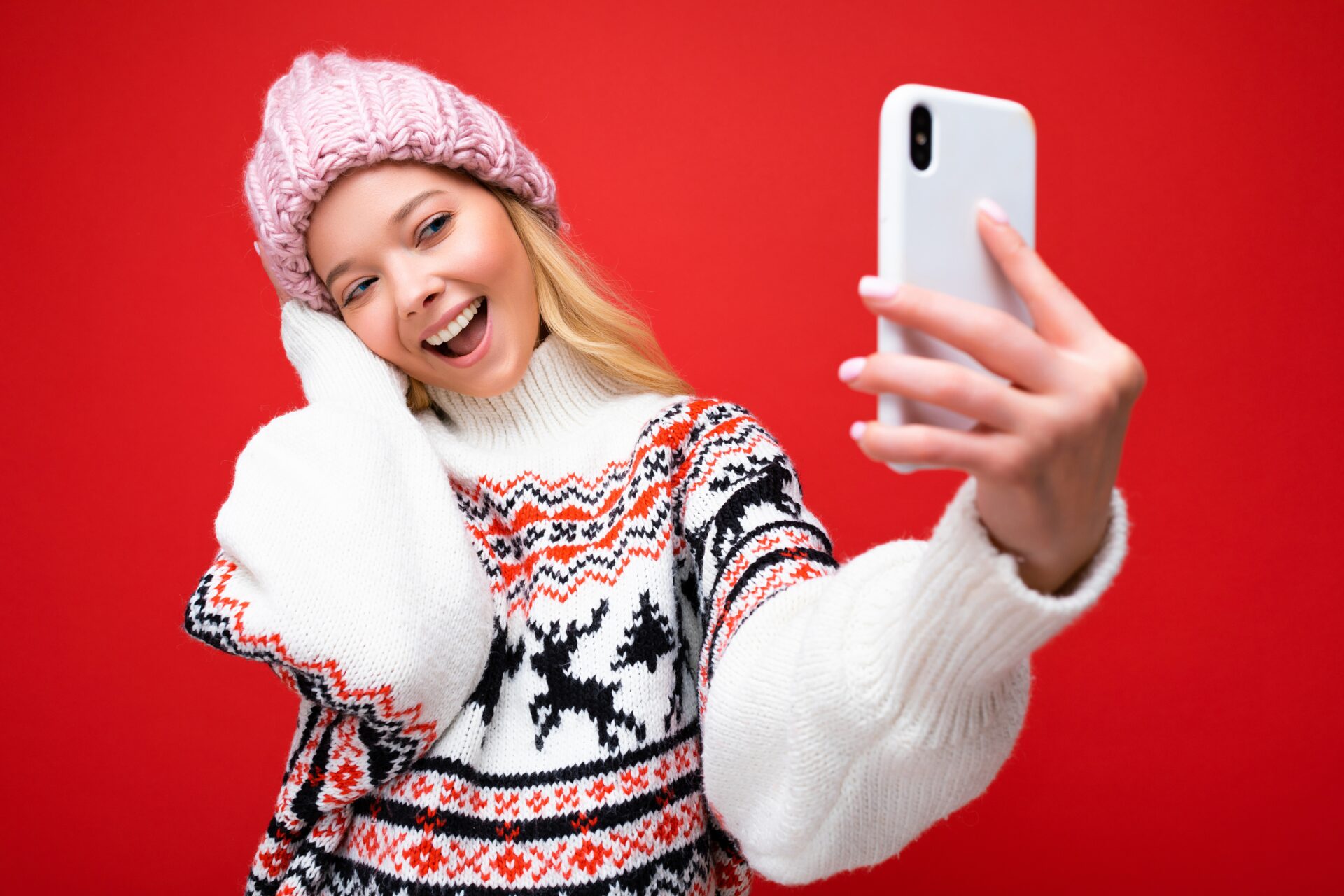 Attractive charming young smiling happy woman holding and using mobile phone taking selfie wearing stylish clothes isolated over wall background.